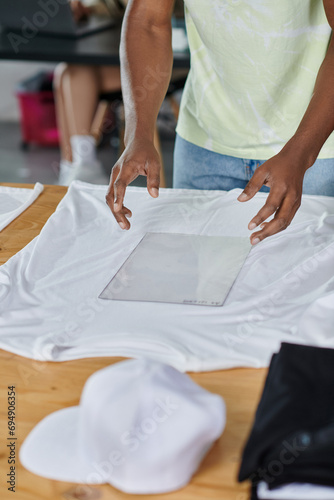 partial view of african american designer holding transparent format template near white t-shirt