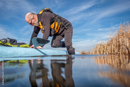 senior male paddler is boarding his stand up paddleboard for paddling workout on a lake