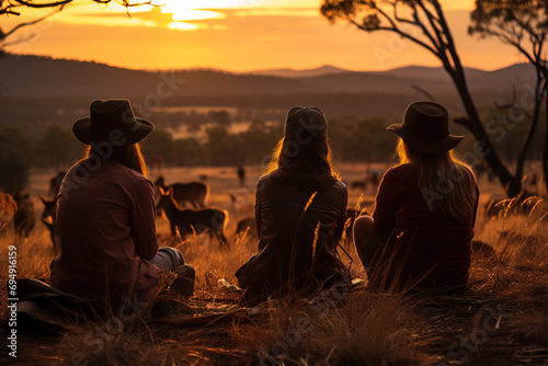Three friends sit in the countryside enjoying a serene sunset  silhouetted against a golden sky.