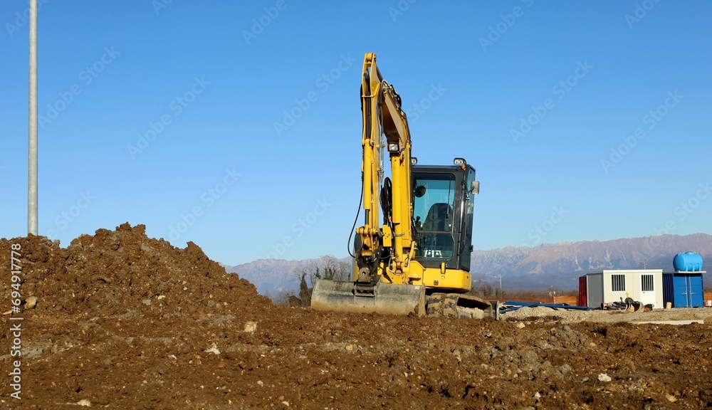 Front view of a mini excavator on heap of dirt in a new housing development area. Front view of a mini excavator on heap of dirt in a new housing development area.