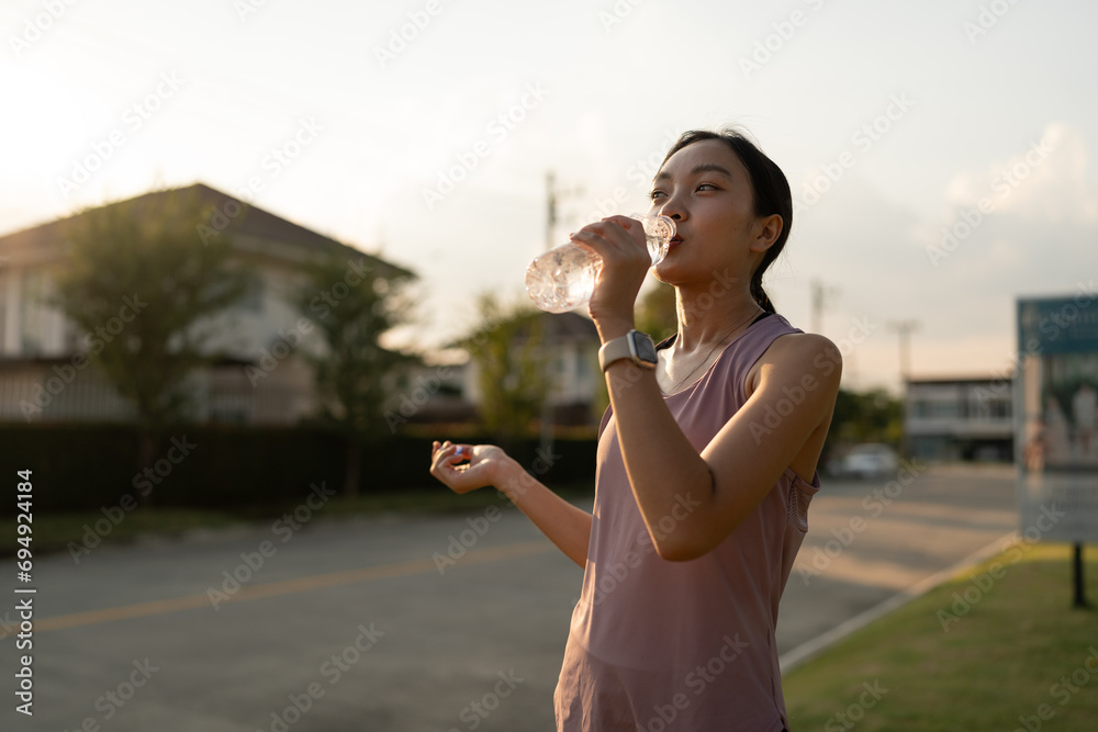 Confident young Asian woman running outdoors along village street. Stand and drink water to cool