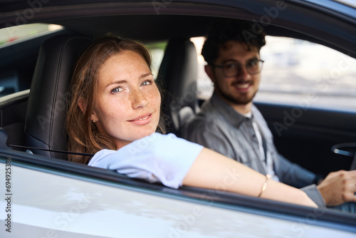 Young smiling caucasian woman and blurred man looking at camera from car window