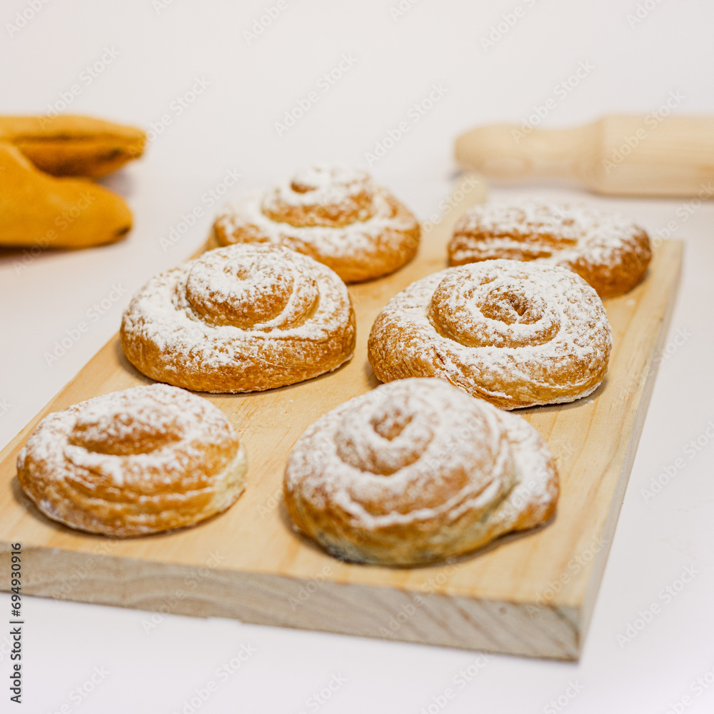 Seis caracolas de pastelería sobre tabla de madera y fondo blanco. 