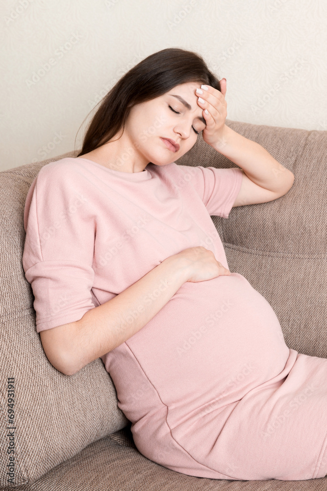 Young pregnant woman suffering from headache on sofa in home. Maternity healthcare concept Young pregnant woman suffering from headache on sofa in home. Maternity healthcare concept