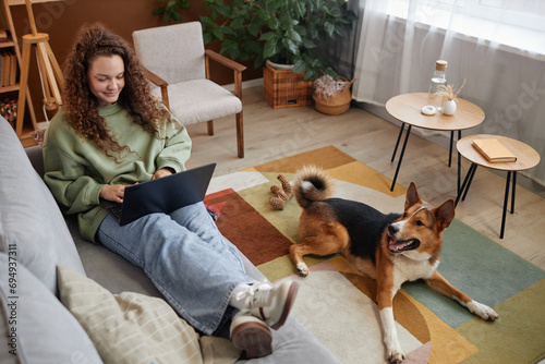 High angle portrait of young woman relaxing on couch with dog waiting happily on floor, copy space photo