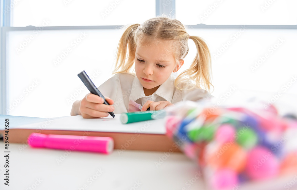Little beatiful schoolgirl with braided hair is sitting at the desk with colorful pencils Little beatiful schoolgirl with braided hair is sitting at the desk with colorful pencils