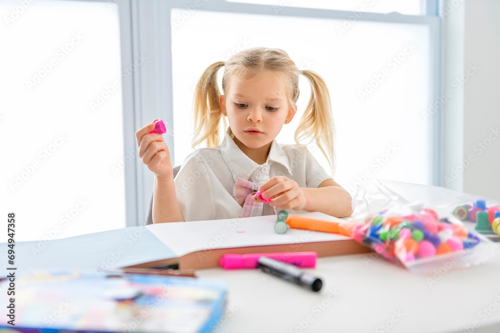 Little beatiful schoolgirl with braided hair is sitting at the desk with colorful pencils Little beatiful schoolgirl with braided hair is sitting at the desk with colorful pencils