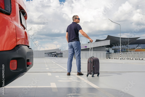 Young man with a suitcase in the airport parking lot. View from the back. Travel concept