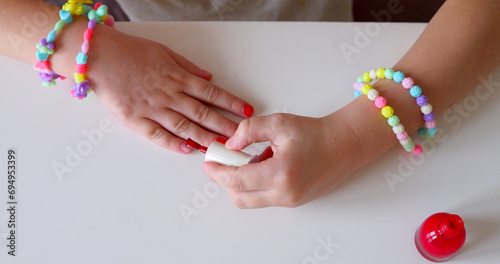 Little girl make manicure and painting nails with red nail polish at home. photo