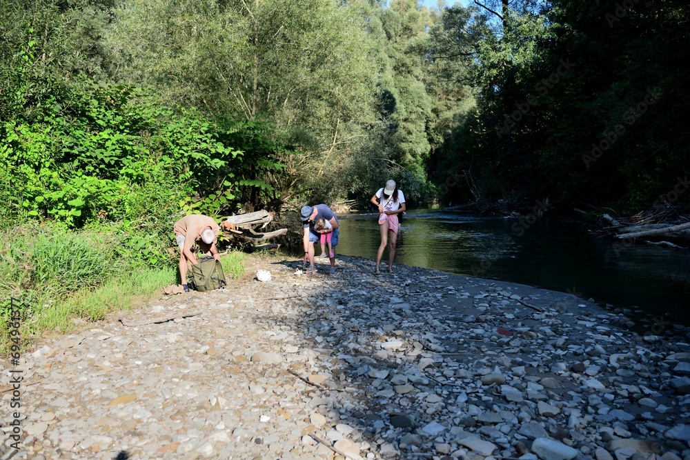 The family is camping by the river and roasting sausage over a natural fire