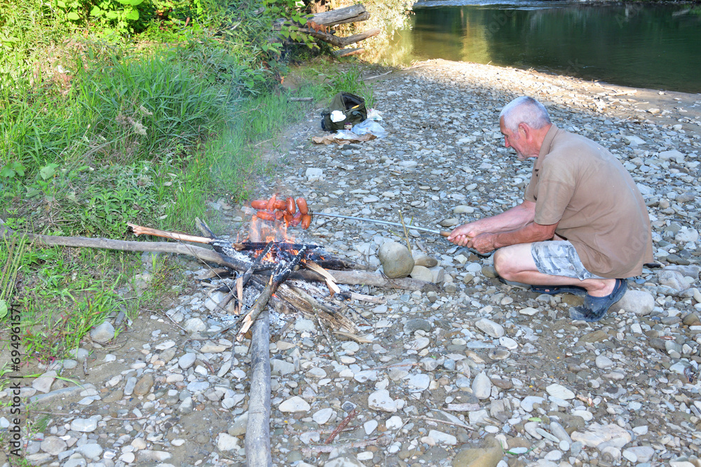 A man roasts a pile of sausages on a stick over a natural fire