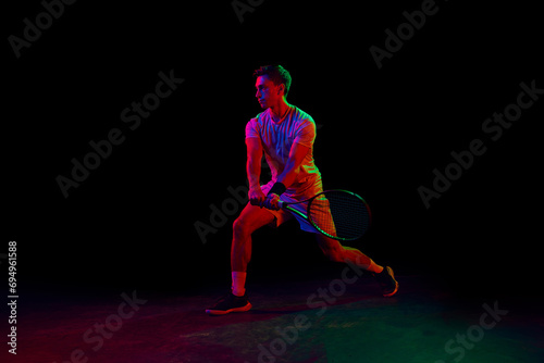 Young man, tennis player during game, playing, practicing against dark background in neon light. Concept of professional sport, competition, game, math, hobby, action
