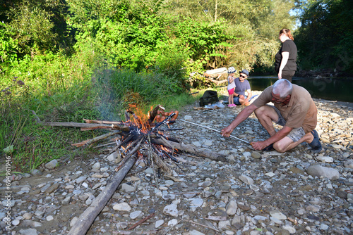 Obraz na płótnie The family is camping by the river and roasting sausage over a natural fire w salonie