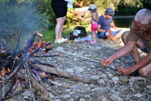 Obraz na płótnie The family is camping by the river and roasting sausage over a natural fire w salonie