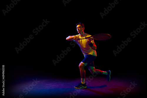 Concentrated athletic man, tennis player in motion, training, practicing against dark background in neon light. Concept of professional sport, competition, game, math, hobby, action