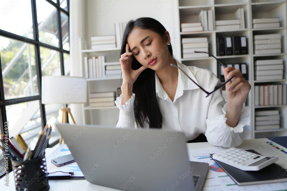 Tired business woman in stress works at a laptop while sitting at a table at home and holds her hand on her temples Tired business woman in stress works at a laptop while sitting at a table at home and holds her hand on her temples