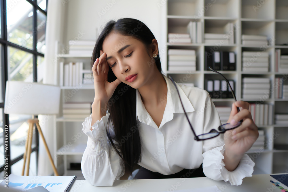 Tired business woman in stress works at a laptop while sitting at a table at home and holds her hand on her temples Tired business woman in stress works at a laptop while sitting at a table at home and holds her hand on her temples