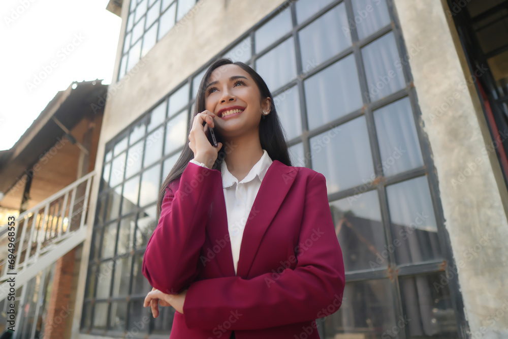 Smiling young Asian business woman wearing suit standing on urban escalator using applications on cell phone, reading news on smartphone, fast connection, checking mobile apps outdoors. Smiling young Asian business woman wearing suit standing on urban escalator using applications on cell phone, reading news on smartphone, fast connection, checking mobile apps outdoors.