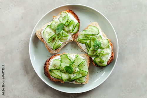 fresh and healthy vegetable appetizer cucumber toast with greek yoghurt mint and basil on a grey minimal concrete background