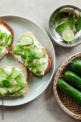 fresh and healthy vegetable appetizer cucumber toast with greek yoghurt mint and basil on a grey minimal concrete background