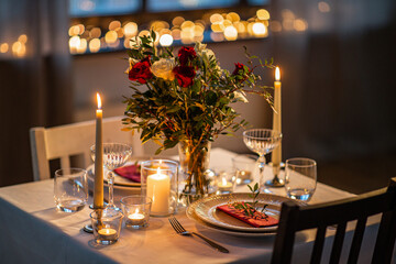 holidays, romantic date and celebration concept - close up of festive table serving for two with flowers in vase and candles burning at home on valentine's day