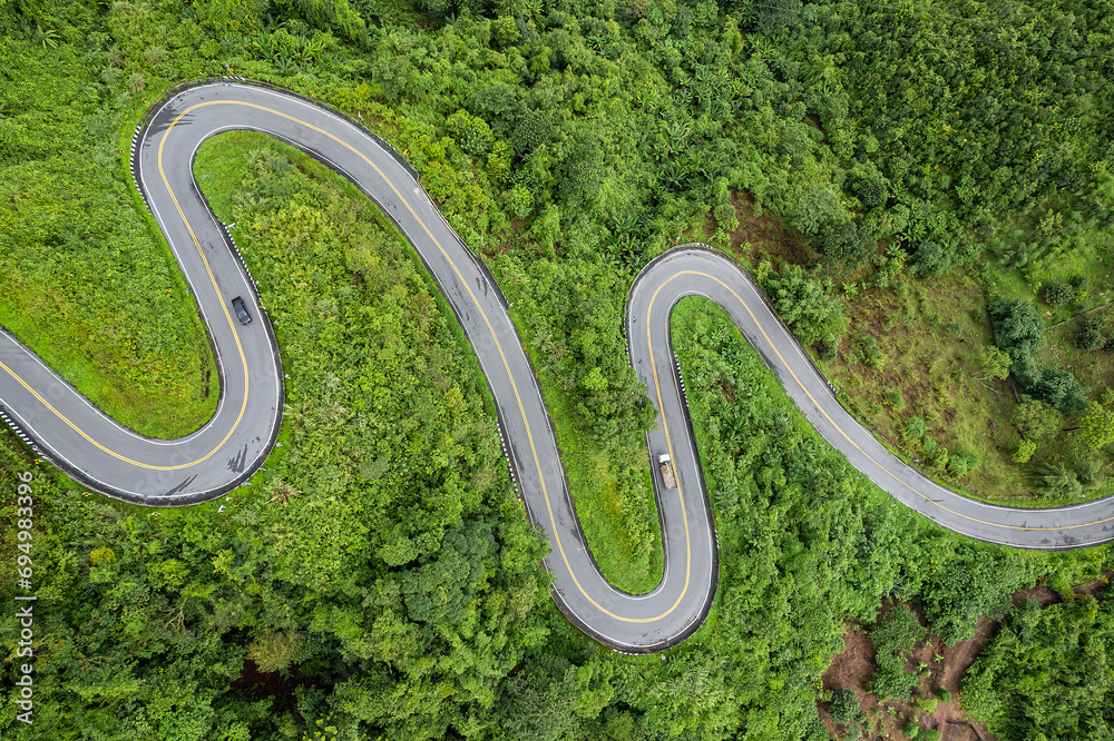 Aerial view of countryside road passing through the green forest and mountain in Thailand.