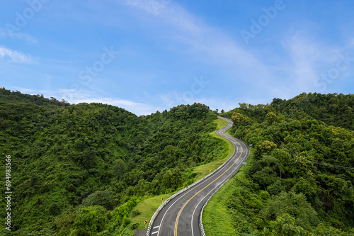 Aerial view of countryside road passing through the green forest and mountain in Thailand.