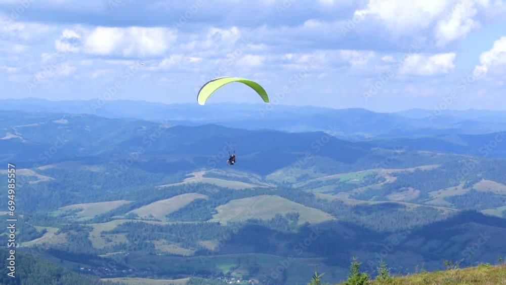 Paragliding instructor and a passenger are flying a paraglider in tandem. Beautiful summer sunny day. High mountain Carpathian landscape. Blue cloudy sky. Paragliding instructor and a passenger are flying a paraglider in tandem. Beautiful summer sunny day. High mountain Carpathian landscape. Blue cloudy sky.