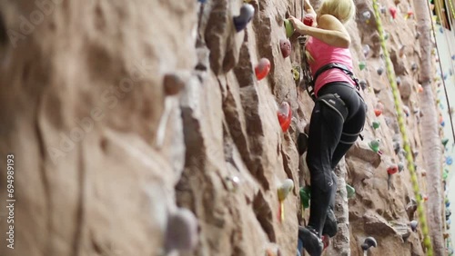 Pretty blonde woman with special equipment climbs on wall photo