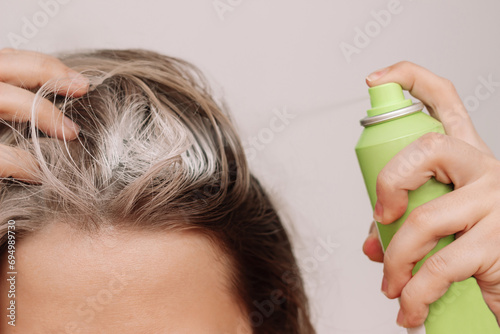 Woman's head with dirty greasy hair. The girl spraying dry shampoo on the roots of her hair on a light background. The problem of oily scalp. A quick way to cleanse photo