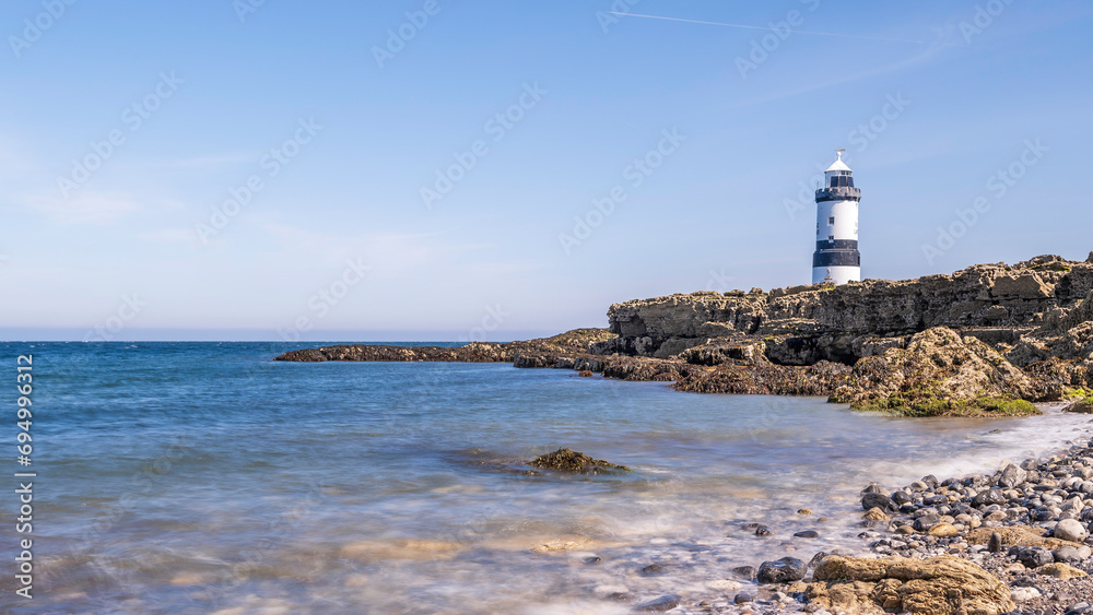 Lighthouse on the edge of a rocky headland.  The lighthouse is located at Penmon Point, Angelsey, north Wales. The day is sunny