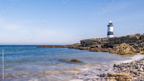 Lighthouse on the edge of a rocky headland. The lighthouse is located at Penmon Point, Angelsey, north Wales. The day is sunny