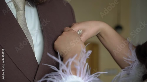 Groom puts on a handkerchief. A girl, a bride or bridesmaid, straightens cloth on a man's suit. Male in a white shirt, tie and jacket. photo