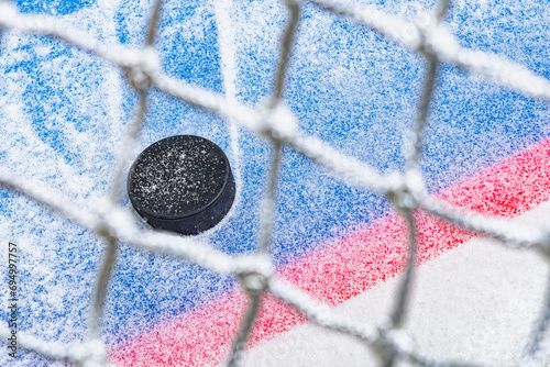 Looking through the net at an ice hockey puck stopping on the edge of the Goal Line of the goal crease. photo