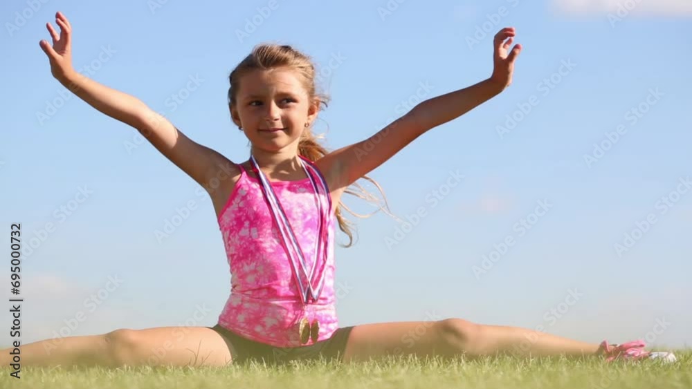 Little girl in shorts splitting legs apart on green grass 