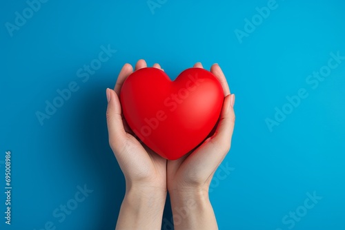 Hands holding a red heart against a blue background.