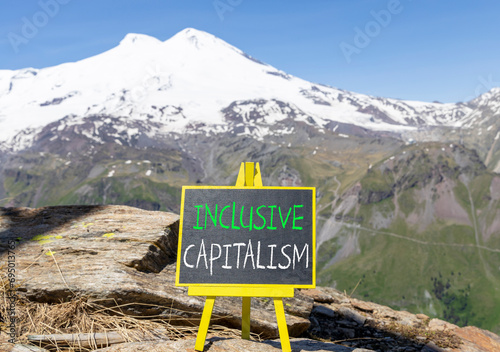 Inclusive capitalism symbol. Concept words Inclusive capitalism on beautiful black chalk blackboard. Beautiful mountain Elbrus blue sky background. Business inclusive capitalism concept. Copy space. © Dzmitry