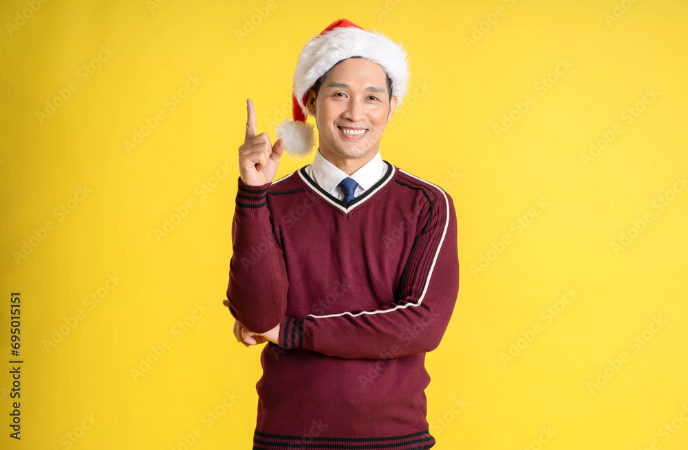 Portrait of an Asian man wearing a Christmas sweater and hat posing on a yellow background Portrait of an Asian man wearing a Christmas sweater and hat posing on a yellow background
