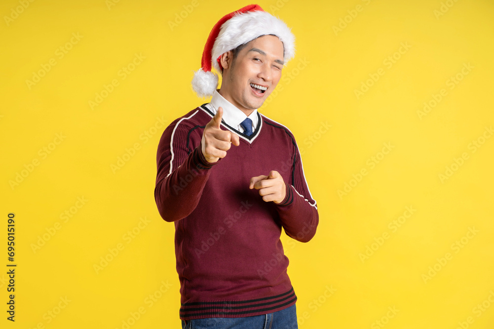 Portrait of an Asian man wearing a Christmas sweater and hat posing on a yellow background Portrait of an Asian man wearing a Christmas sweater and hat posing on a yellow background
