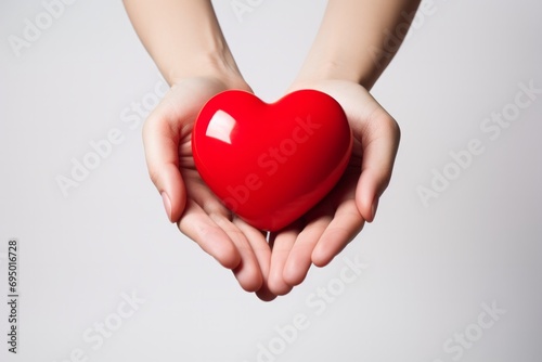 Hands holding a red heart against a white background.