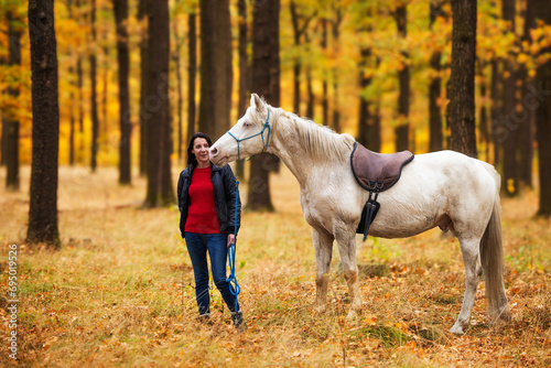 A pretty young woman and a white horse standing together in the autumn forest © michal