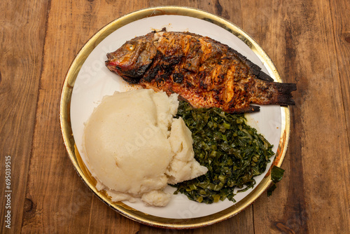 Whole grilled tilapia, accompanied by traditional African food (ugali) and stir-fried kale