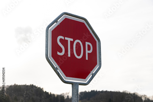 Red and white stop sign in front of a gray sky with forest, close up view, photographed from the left side, without people during the day