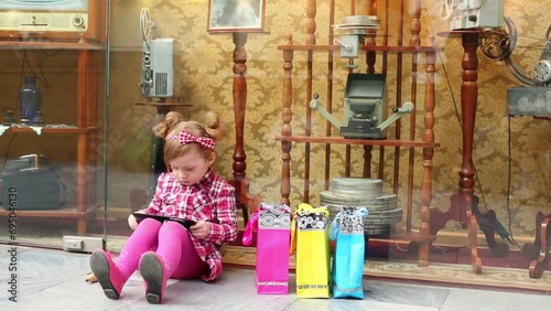 Little girl sits on floor and looks at tablet pc near showcase