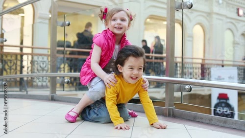 Little girl and boy play on floor in big mall. Girl saddled boy photo