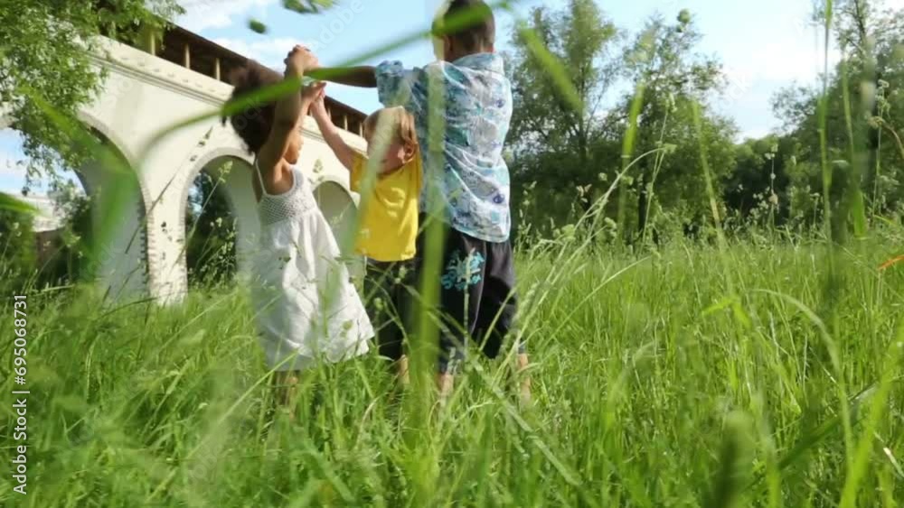 Girl and two little boys play in grass of park near aqueduct