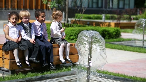 Four children in business clothes sit on bench near fountain photo