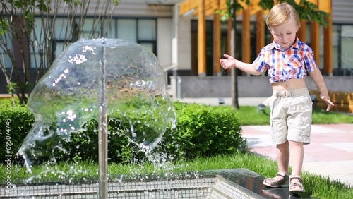 Little cute boy is trying to get leg to water in fountain  photo