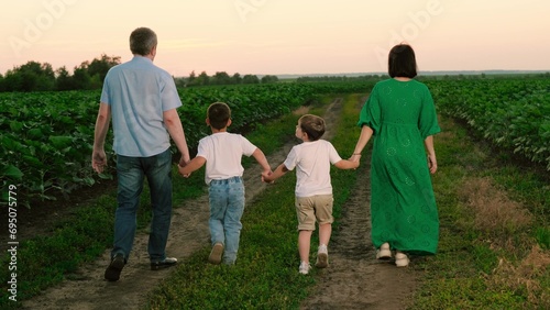 Family walks across country land with children spending vocation together. Children enjoy happy childhood with family. Happy family has walk with small children on plantation at evening dusk