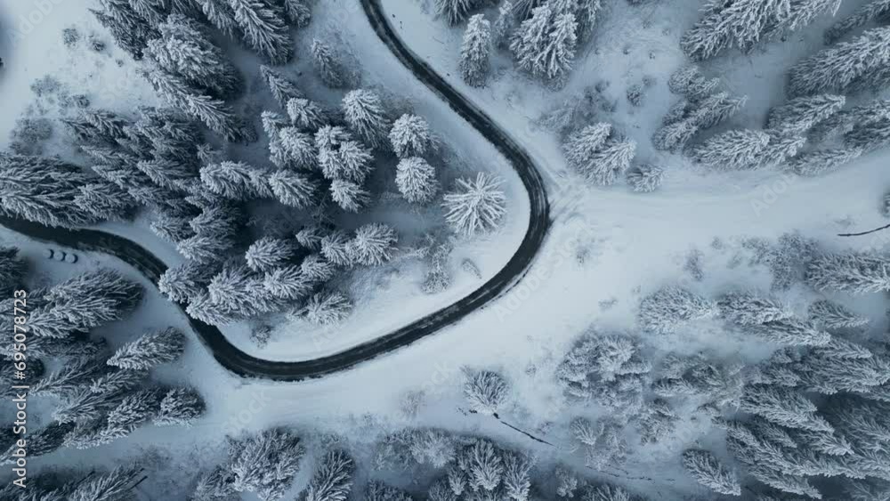 Winter snow road in the middle of pine trees top down aerial view. Snowy landscape from above in the mountains